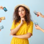 Thoughtful African-American woman and hands with credit cards on color background